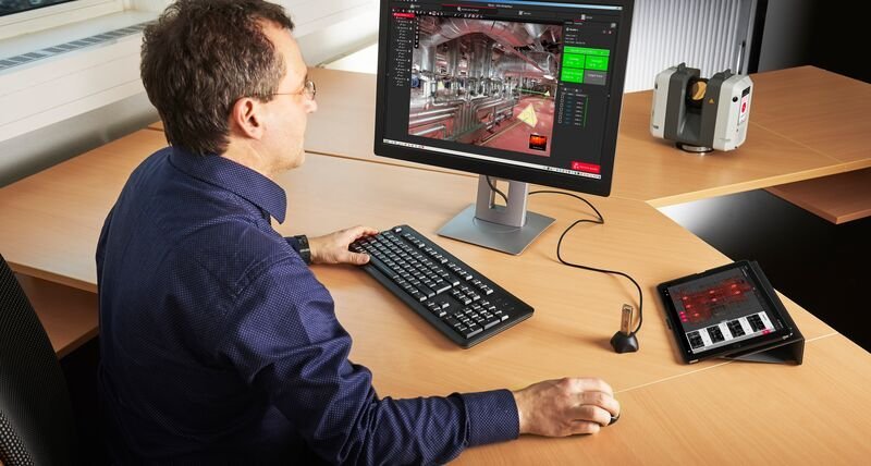 Technician registering a point cloud of an industrial facility's piping and interior in Leica Cyclone software, RTC360 scanner on desk